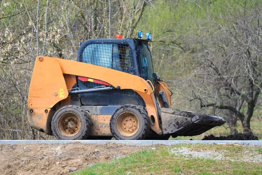 Orange skid steer with a bucket attachment on a wooded lot