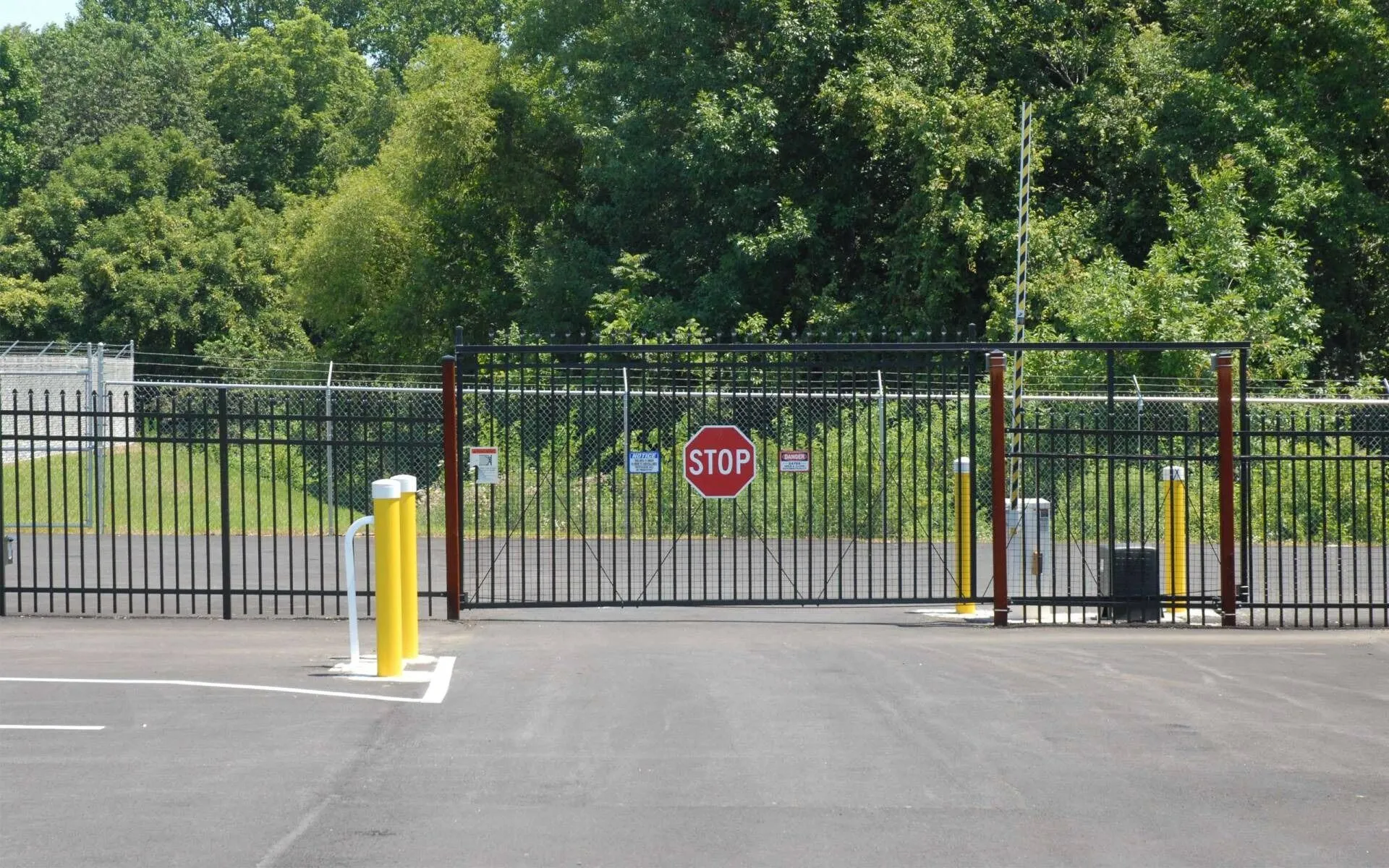 Black steel security gate with a stop sign across a commercial lot entrance