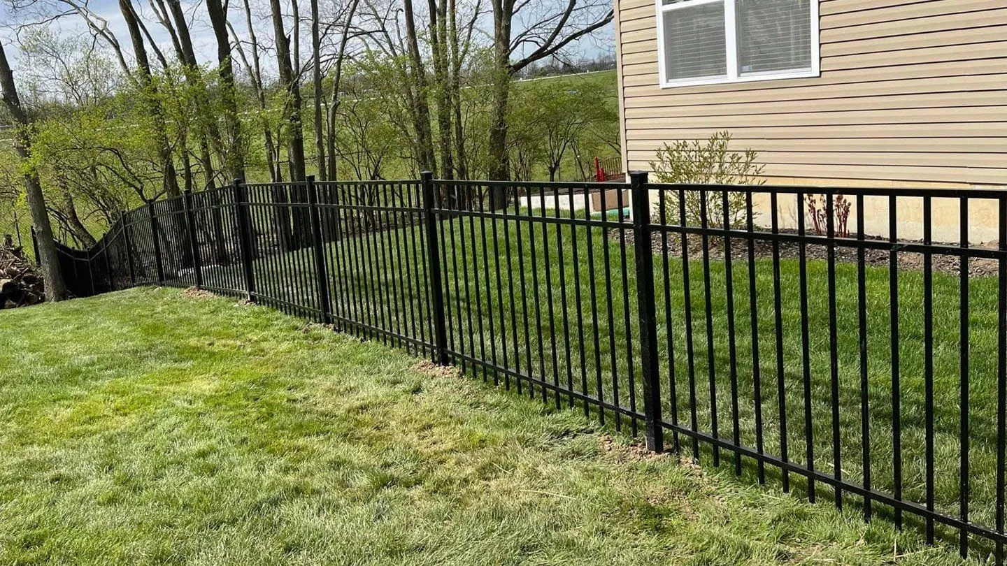 A black  steel fence surrounds a lush green lawn in front of a house.