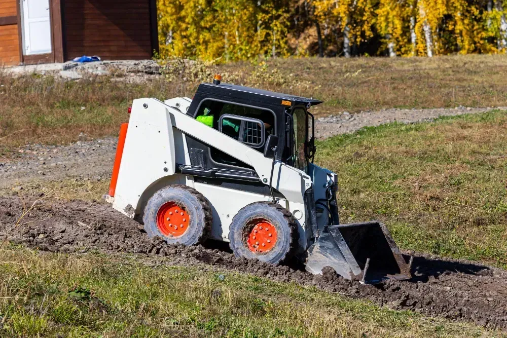 White skid steer grading soil across a yard